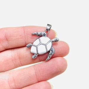 Detailed close-up of a silver turtle pendant with white enamel and sparkling crystals