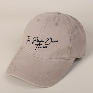 Detailed close-up of blue embroidery and curved stitching on the beige baseball cap