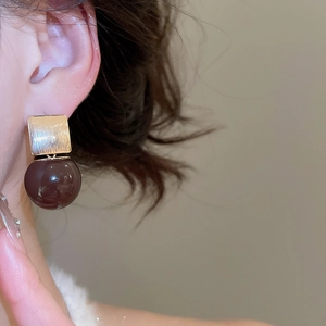 Close-up of model wearing gold brushed metal and dark brown resin sphere drop earrings