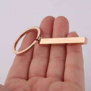 Macro detail of a hand holding a polished rose gold rectangular bar pendant keychain