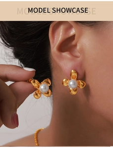 Detailed macro view of gold-plated flower earrings with white pearl centers on model