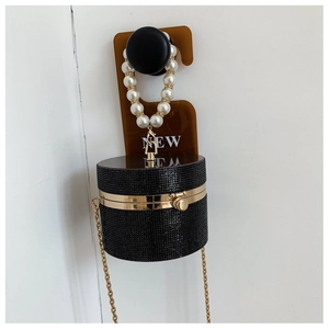 Detail of black cylindrical evening bag with rhinestones, pearl handle, and gold chain