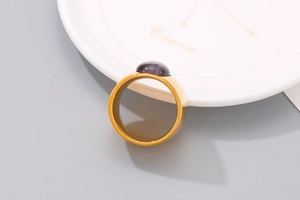 Detail eines goldenen Titanstahlrings mit violettem Katzenaugenstein auf einem Keramikteller