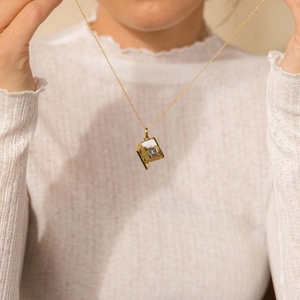 Detail of a golden locket necklace opening to reveal a small photo on a model