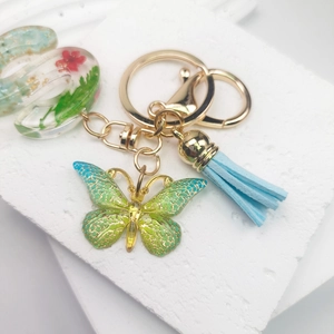 Macro view of green crystal butterfly keychain with blue tassel and dried flower letter charm