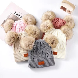 Flat lay of cable knit kids hats with dual pom-poms and leather patch in multiple colors