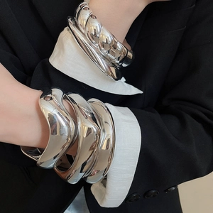 Close-up of polished silver irregular wavy metal bracelets styled on a model's arm