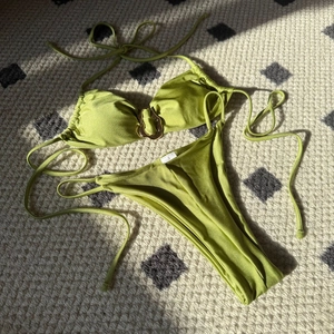 Flachbild eines olivgrünen Glanz-Bikinis mit goldenem Wellenring und glatter Textur