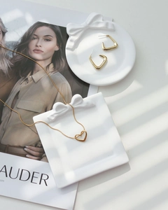 Close-up of golden heart necklace and square earrings on a plaster bow tray with soft shadows