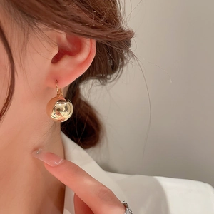 Gros plan d'une boucle d'oreille en boule dorée portée par un mannequin sous une lumière douce