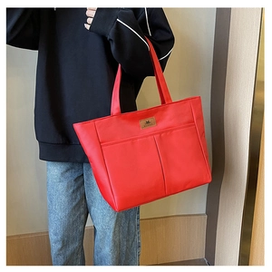Detail view of red tote bag with two front pockets shown on model for daily casual wear