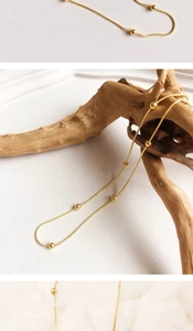 Detail of 18K gold-plated beaded snake chain necklace displayed on a natural wood piece