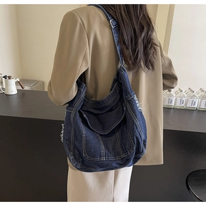 Gros plan d'un sac à bandoulière en denim bleu avec coutures vintage et détails effilés