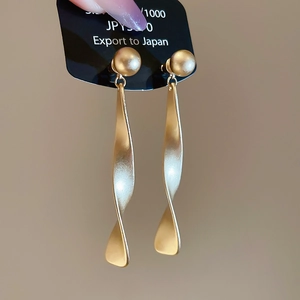 Vue détaillée de boucles d'oreilles pendantes géométriques en spirale dorée mate et perle