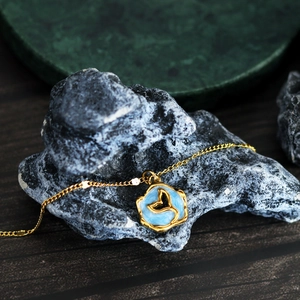 Elegant gold fish tail necklace with blue enamel pendant on dark stone background