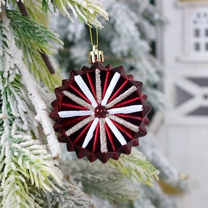 Red star-shaped Christmas ornament with glitter stripes hanging on a snowy tree branch