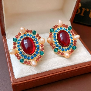 Detail of vintage gold earrings with red, blue, green stones and pearls in a leather box