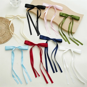 Elegant satin bow hair clip with long ribbons in multiple colors on a wooden tray