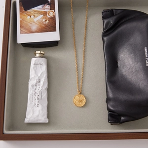 Close-up of 18K gold stainless steel necklace with coin bee pendant on a wooden tray