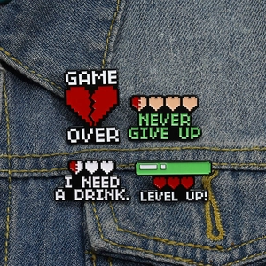 Detail showing pixel art enamel pins with game over motifs on blue denim jacket