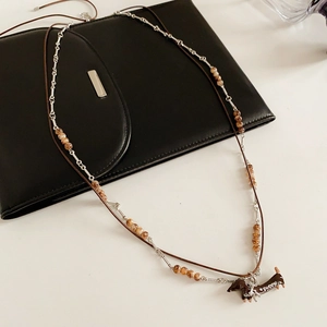 Close-up of dachshund puppy pendant on layered leather cord and silver beaded necklace