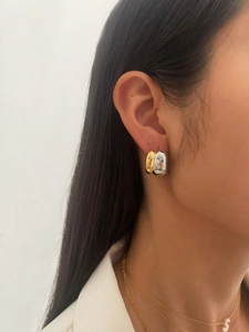 Detail of two-tone C-shape hoop earrings and gold letter S necklace on a model