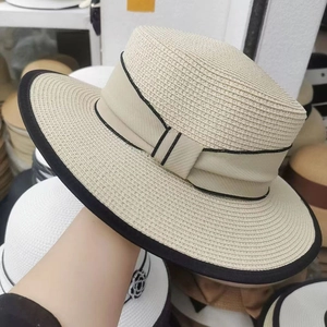 Close-up of beige straw boater hat with black ribbon edge and textured flat top weaving