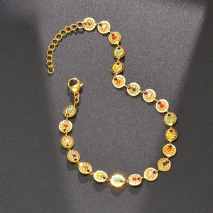 Detail of gold chain bracelet with colorful beads and textured discs on a matte background