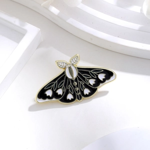 Detail of moth enamel brooch with white floral patterns and gold-toned metal outlines
