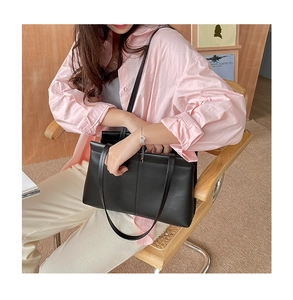 Chic black leather tote bag shown on a model sitting in a stylish cafe setting