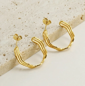 Macro shot of 18k gold wave hoop earrings on a textured stone surface with stud closure