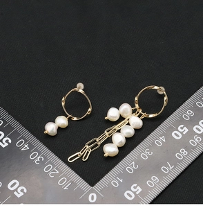 Detailed view of asymmetric natural pearl tassel earrings in gold plating on black background