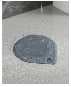 Dettaglio del copriscarico in silicone grigio con schizzi d'acqua su piano in quarzo