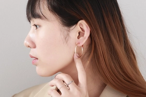 Close-up of rose gold oversized hoop earrings and silver stacking rings on a model