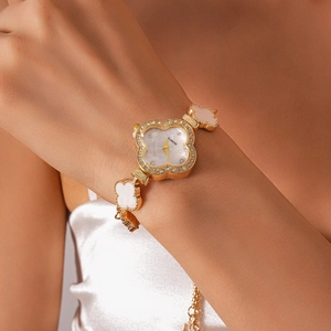 Close-up of golden four-leaf clover watch bracelet with clear rhinestones on white dial