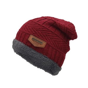 Détail du bonnet en tricot rouge avec doublure en fourrure grise et écusson en cuir