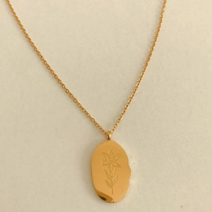Gros plan détaillé du pendentif fleur ovale irrégulier double face sur une chaîne dorée