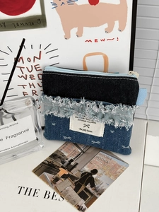 Detail of multi-tone denim coin purse with zipper closure and frayed fabric texture