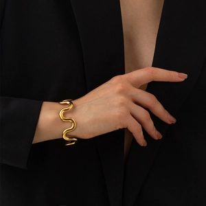 Close-up of wavy 18k gold-plated stainless steel bangle on a model in a black suit