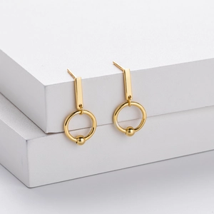 Detail of geometric gold drop earrings featuring a vertical bar and round bead on white cubes