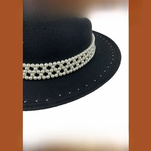 Detalle de sombrero de lana negro vintage con malla de perlas triple y remaches metálicos