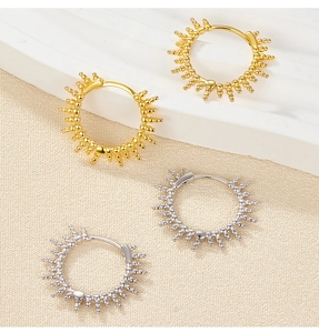 Detailed view of gold and silver sun-shaped hoop earrings on elegant textured fabric
