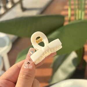 Detail of cream mini claw clip with golden spring held against natural outdoor background
