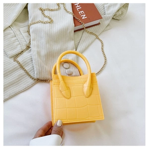 Detail of yellow crocodile embossed mini bag with gold chain strap on knitted texture