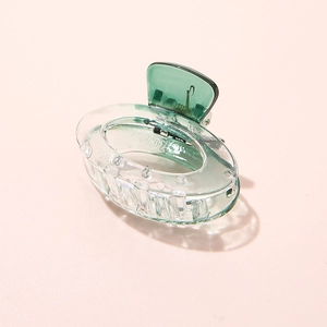 Detail view of a small transparent green oval acetate hair claw clip on pink background