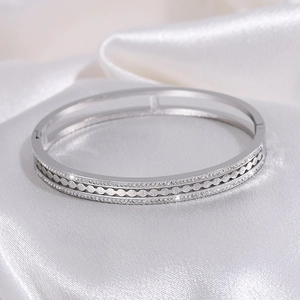 Detailed macro view of silver steel bangle with wavy patterns and inset zircons on silk