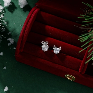 Macro shot of asymmetric Christmas reindeer and gift box stud earrings in a red velvet box