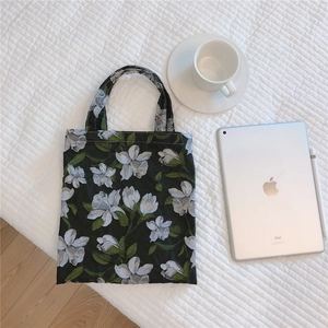 Detail view of a black cotton tote bag with white floral patterns on white bedding