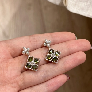 Detailed shot of clover earring with green gems, pearls and diamonds in hand