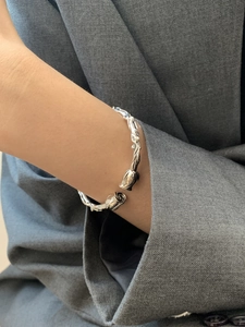 Detailed view of silver rose and thorn bangle worn on wrist over a grey suit sleeve